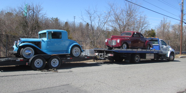 A tow truck towing two old cars on the back of it.