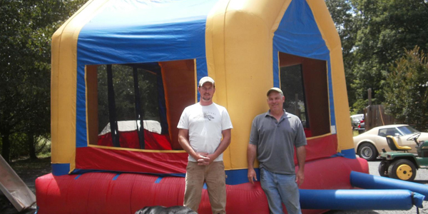Two men standing in front of a bouncy house.