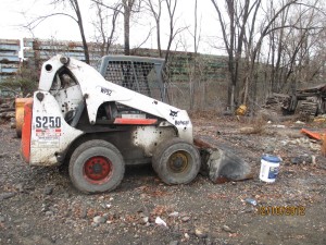 A white and black skid steer is parked in the dirt.
