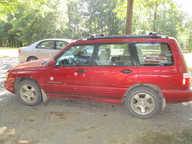 A red car parked in the dirt near trees.