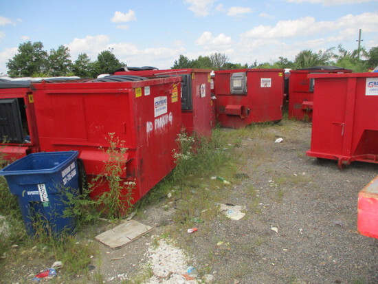 A bunch of red trash cans sitting in the grass.